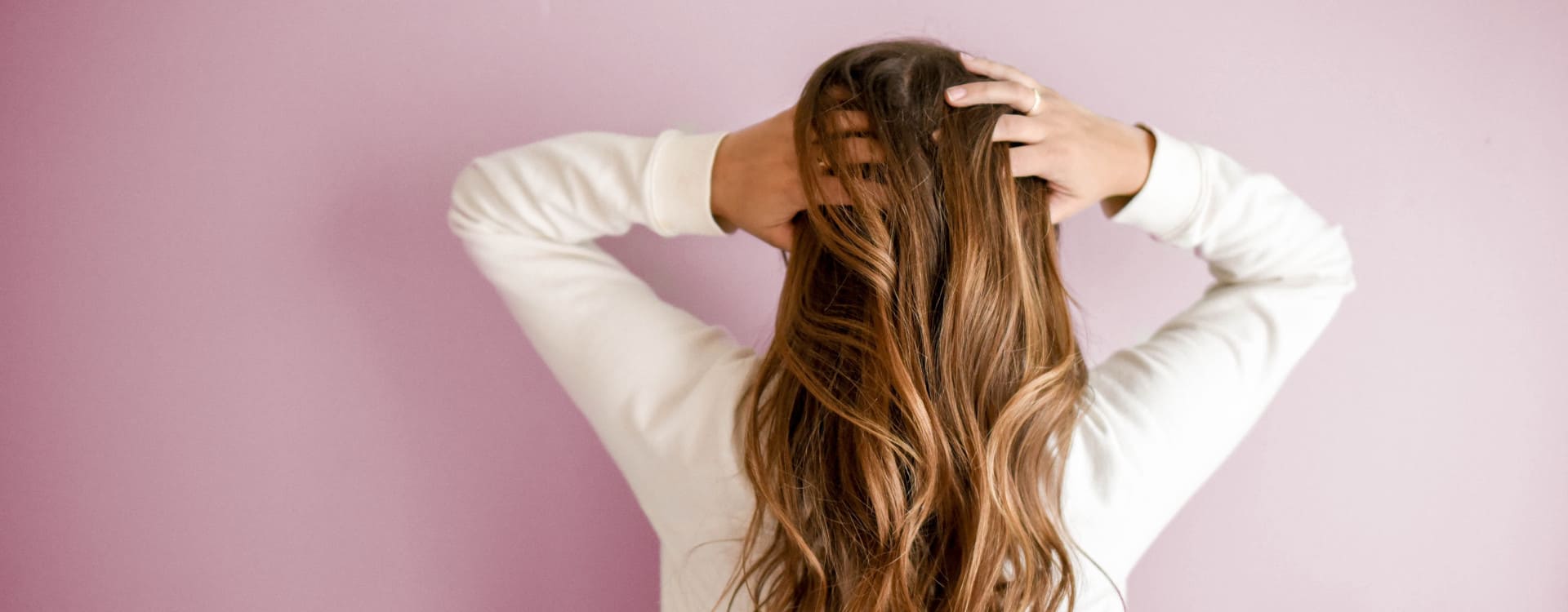 Come capire se la caduta dei capelli è normale? - Una donna di spalle e in piedi davanti a un muro rosa si tocca i capelli